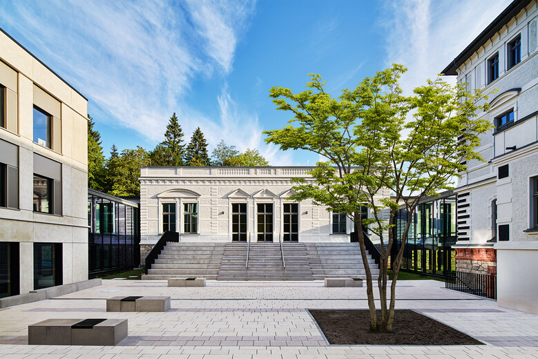 Außenanlage zwischen zwei Gebäuden vor einem weißen Haus mit großen Fenstern
