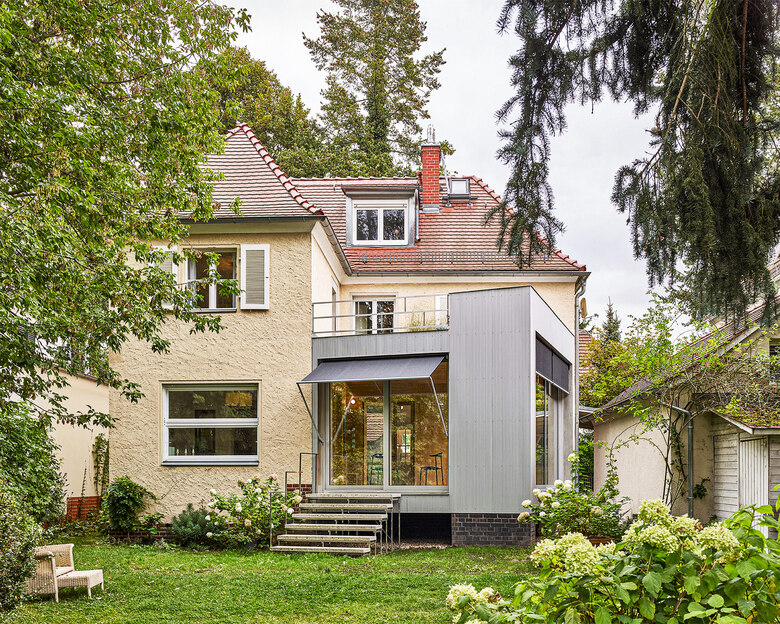 Altes Gebäude mit modernem Anbau in grau, grüner Garten im Vordergrund