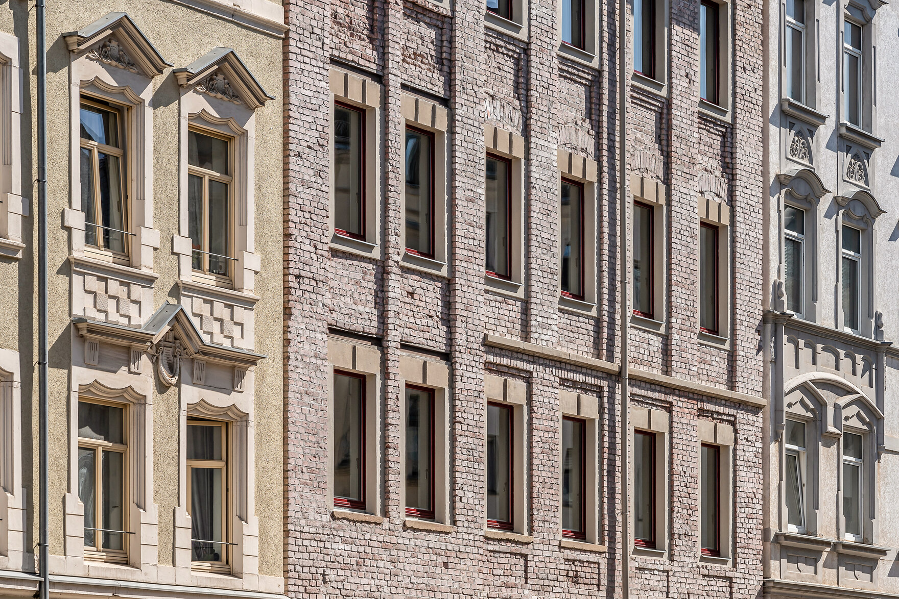 Alte Reihenhäuser, alle aus verschiedenen Materialien, in der Mitte ein aus rosafarbenem Backstein