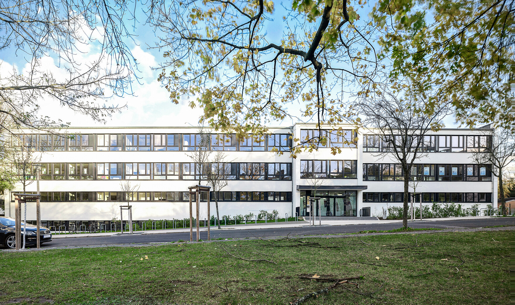 Großes Schulgebäude mit Fenstern im Vordergrund eine Straße und Wiese