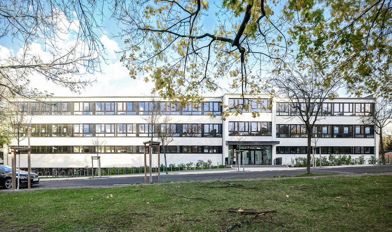 Großes Schulgebäude mit Fenstern im Vordergrund eine Straße und Wiese